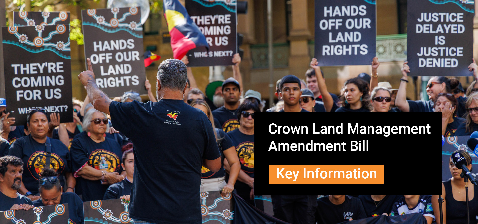 Protest crowd holding signs that read 'They're coming for us' and 'Hands off our land rights' with a speaker addressing the group, plus a bold banner about Crown Land Management Amendment Bill and a 'Key Information' callout.